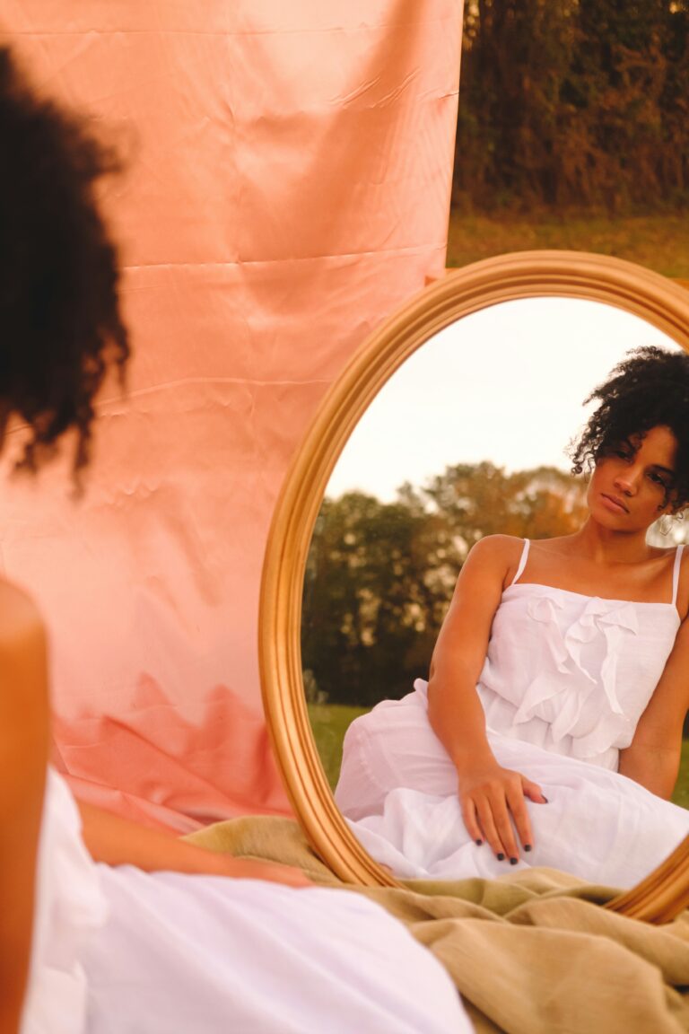 A woman looks in the mirror as she sits in a peaceful environment. This represents choosing yourself. Finally seeing yourself for the first time., acing truth, growth, accountability, and healing